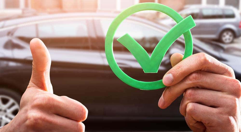 Hand holding up a checkmark symbol near a black car.