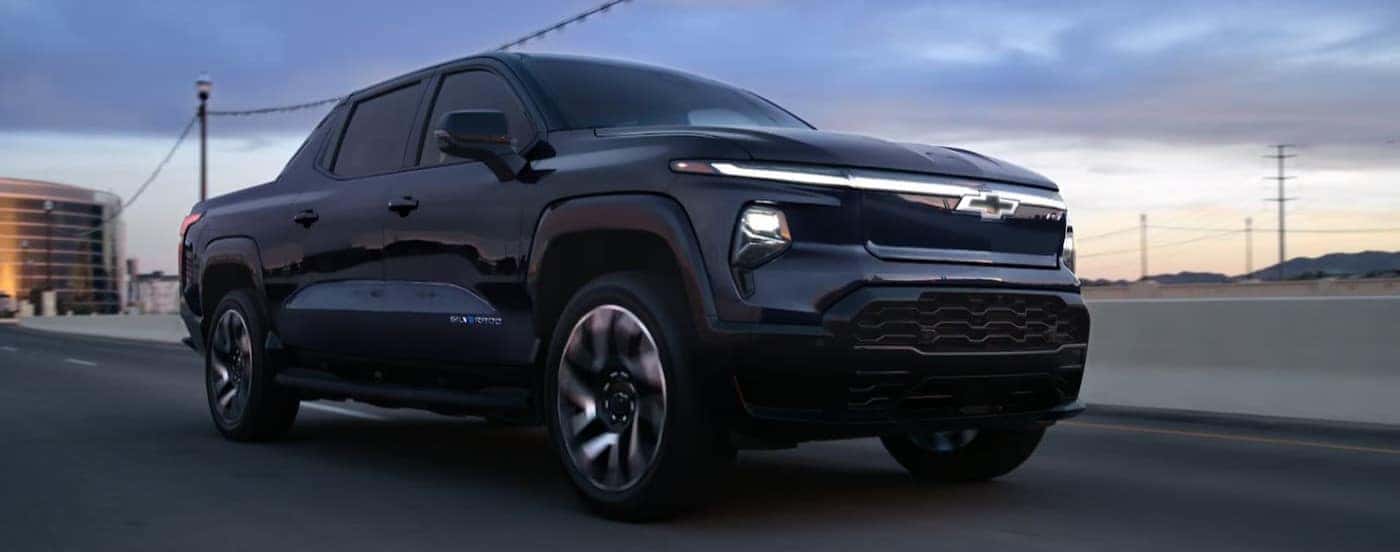 A black 2025 Chevy Silverado EV driving on a city street.