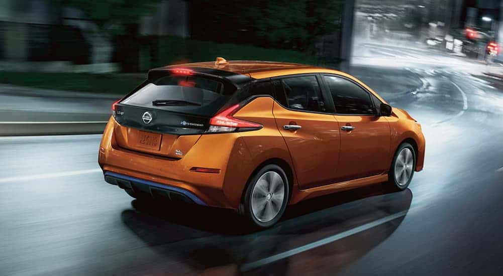 An orange 2021 Nissan LEAF driving after viewing used cars for sale near Newport.