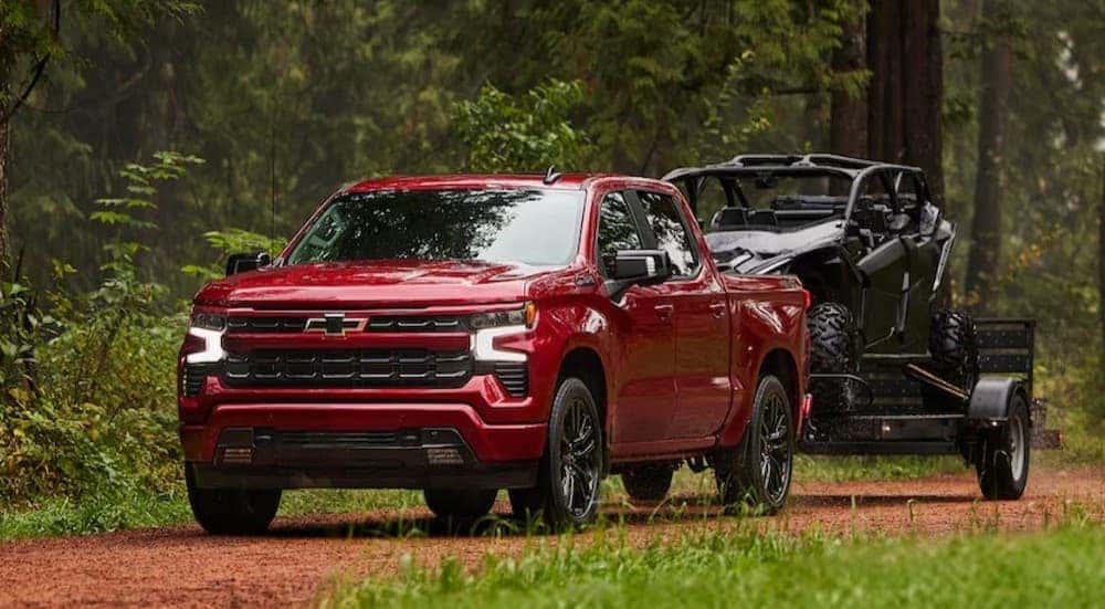 A red 2025 Chevy Silverado 1500 RST towing a trailer on a dirt path.