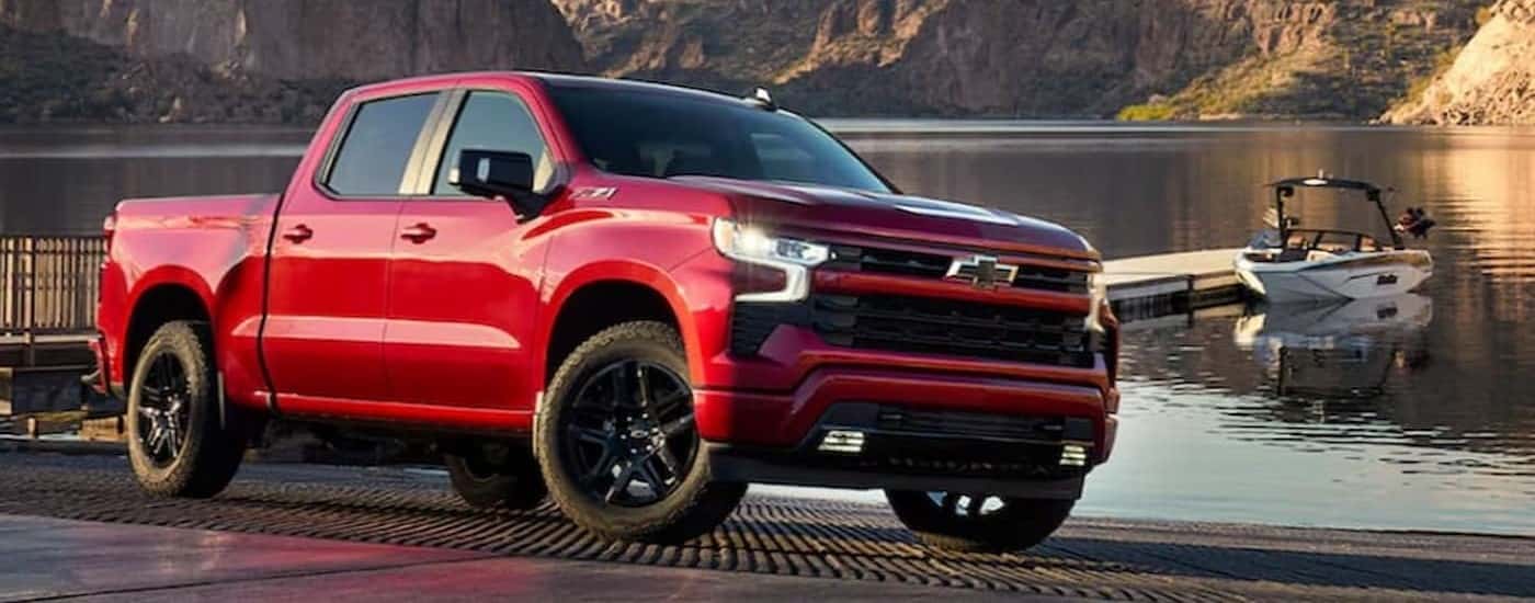 A red 2025 Chevy Silverado 1500 RST parked near a docked boat.