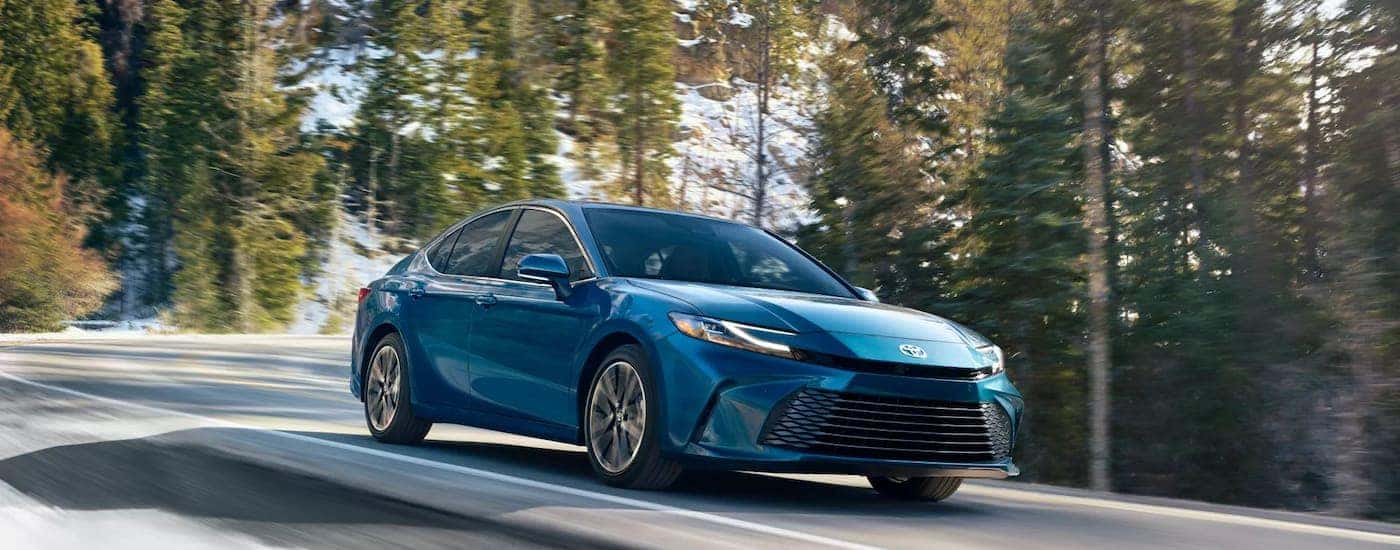 Blue 2025 Toyota Camry driving around a bend from a Toyota service center near Covington.