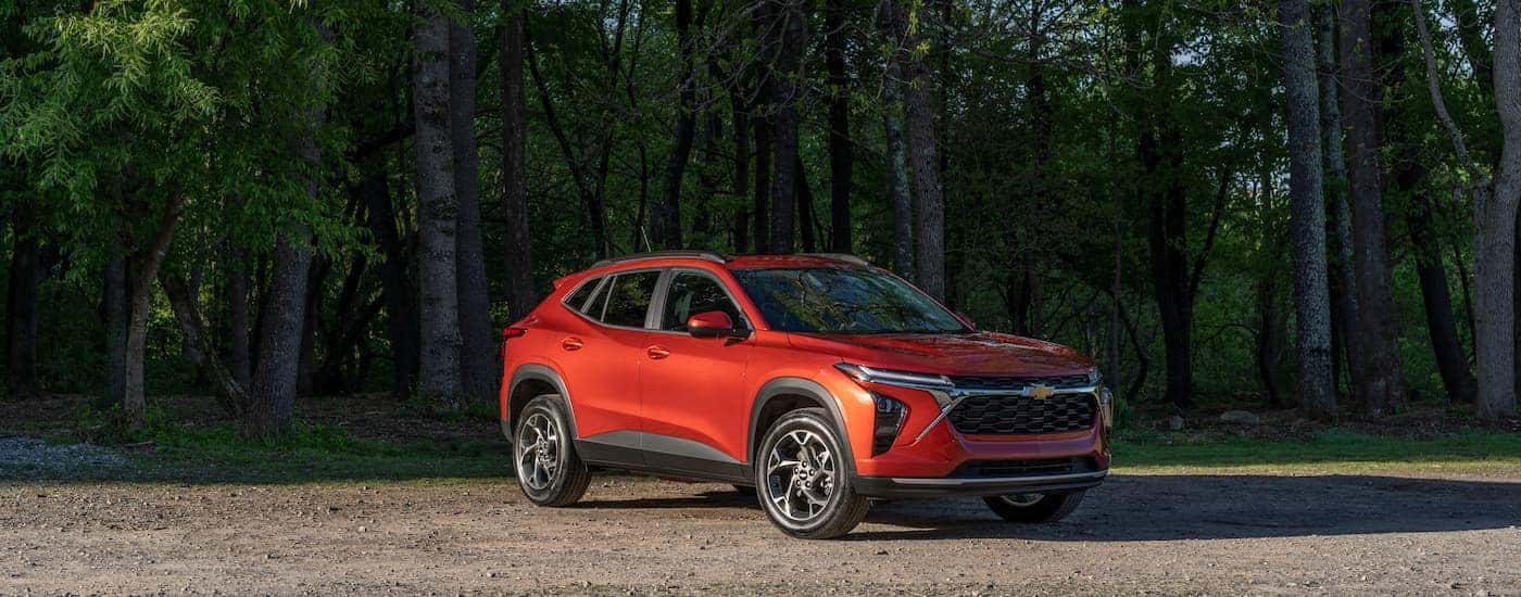 Orange 2025 Chevy Trax parked on dirt surrounded by trees