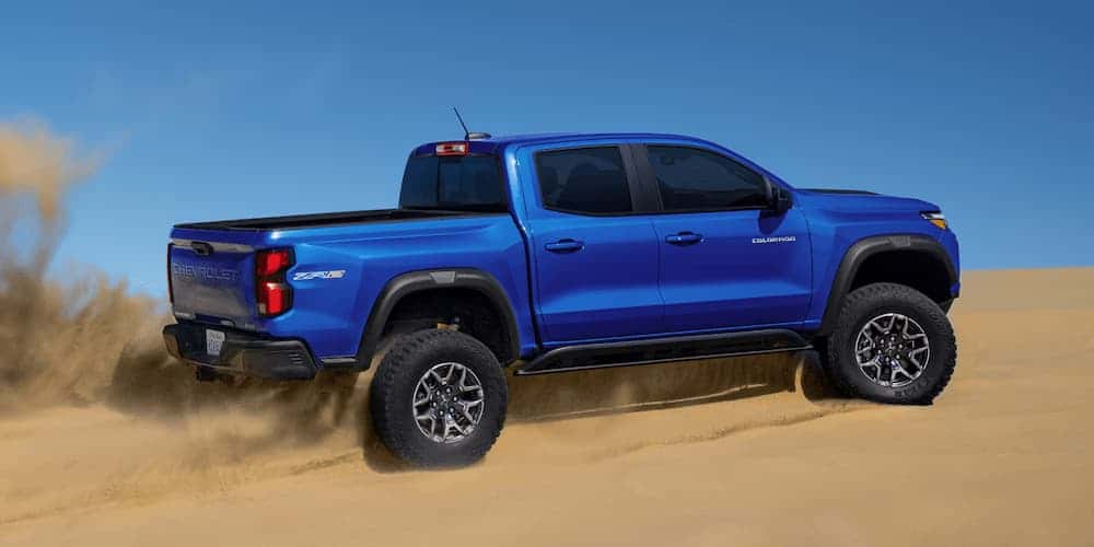 Blue 2025 Chevy Colorado from the side driving up a sand dune.