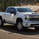 White 2025 Chevy Silverado 2500 driving down the road for sale in Cincinnati.
