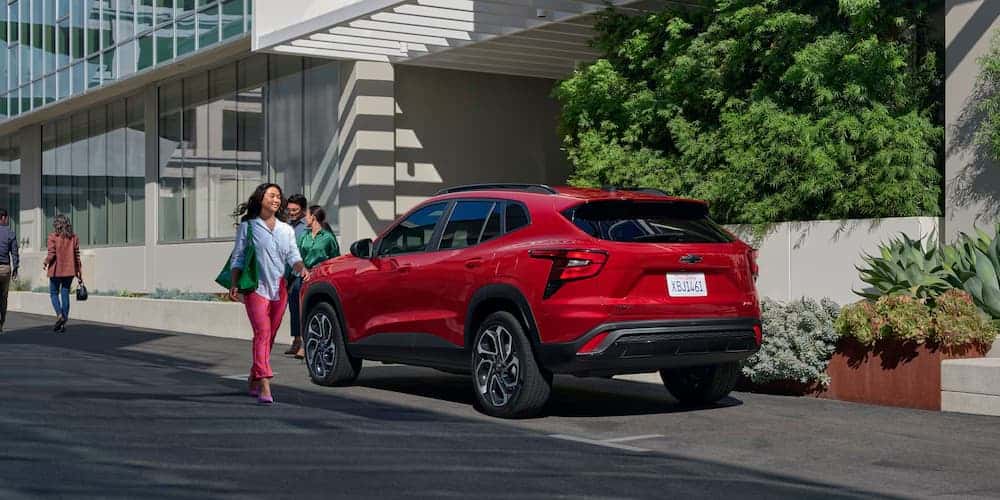 A person walks away from a red 2026 Chevy Trax parked on the curb.