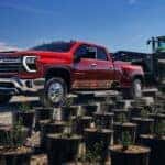 Red 2025 Chevy Silverado 2500 HD from the side towing a tractor down the street.