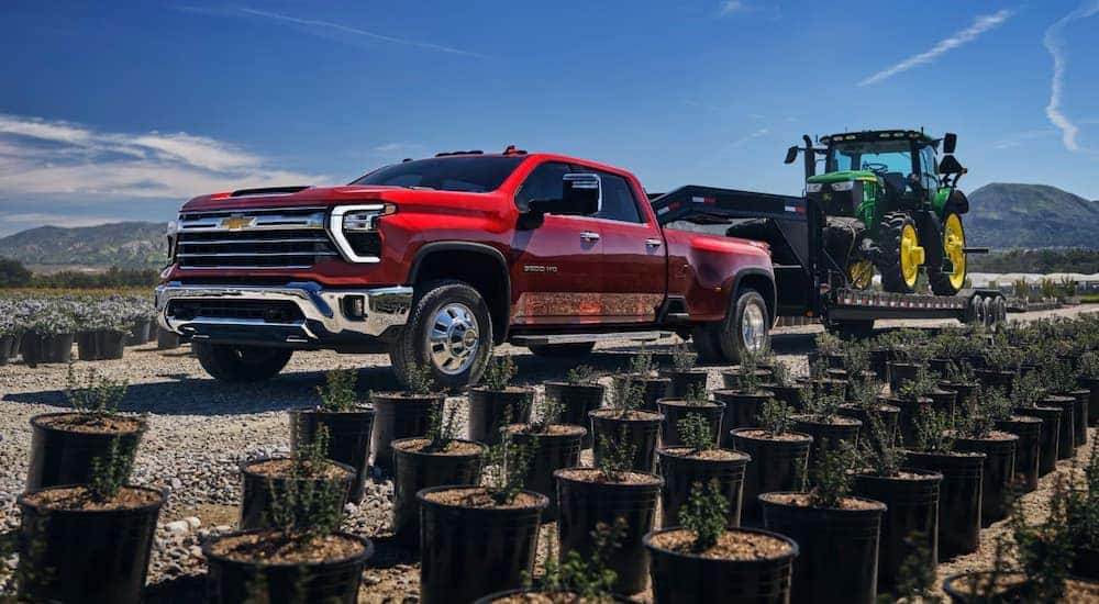 Red 2025 Chevy Silverado 2500 HD from the side towing a tractor down the street.