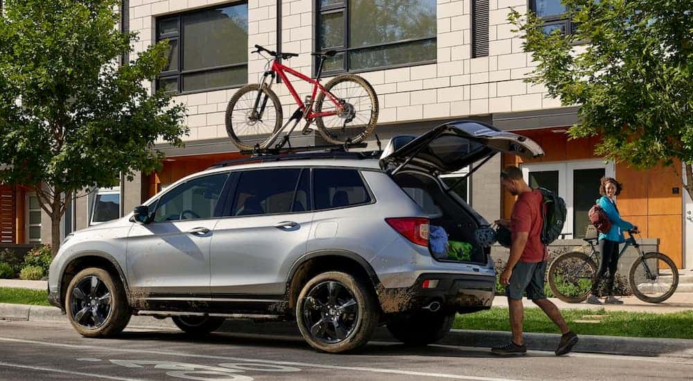 2025 Silver Honda Passport parked on a city street as a person loads the trunk.