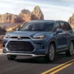 2024 Toyota Grand Highlander driving down an empty road in the desert.