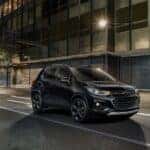 Black 2018 Chevy Trax driving down a city street at night from the side.