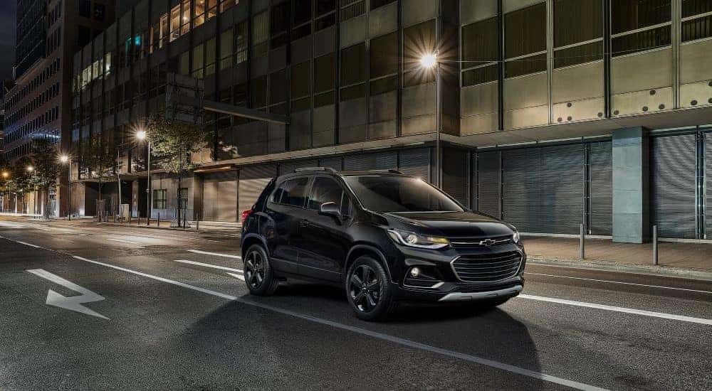 Black 2018 Chevy Trax driving down a city street at night from the side.
