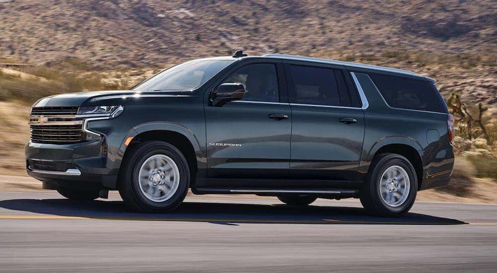 Dark grey 2021 Chevy Suburban from the side driving down the road.