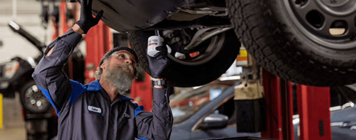 A Ford Mechanic at a service center near Monroe looking at the underside of a car on a lift