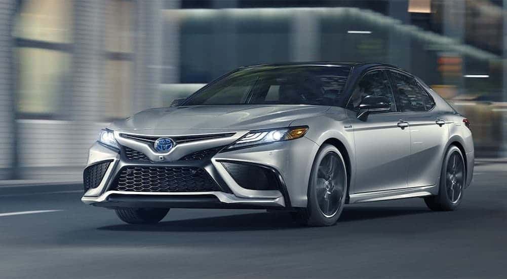 A silver 2021 Toyota Camry Hybrid driving in a city.