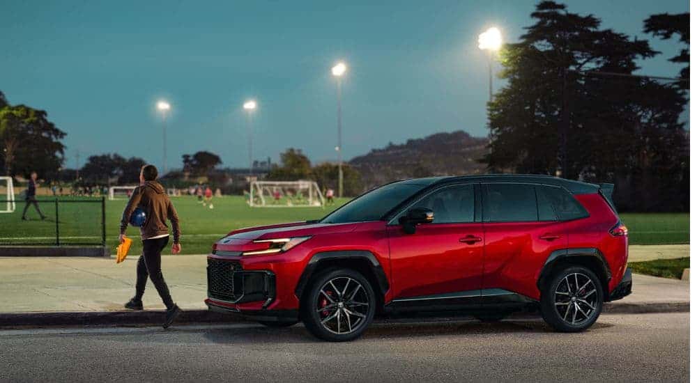 A red 2026 Toyota RAV4 Hybrid parked near a soccer field.