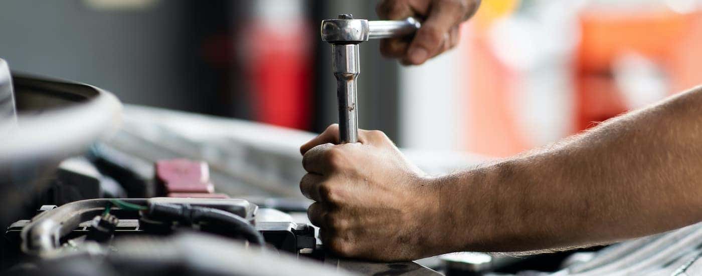 A person tighten a bolt under the hood of their vehicle