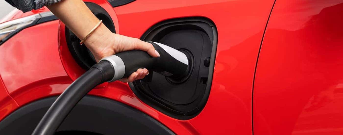 A person charging a red 2027 Chevy Bolt.