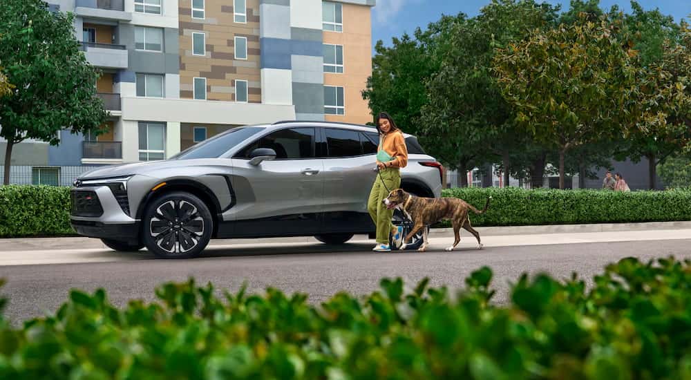 Person walking a dog near a parked silver 2026 Chevy Blazer EV.