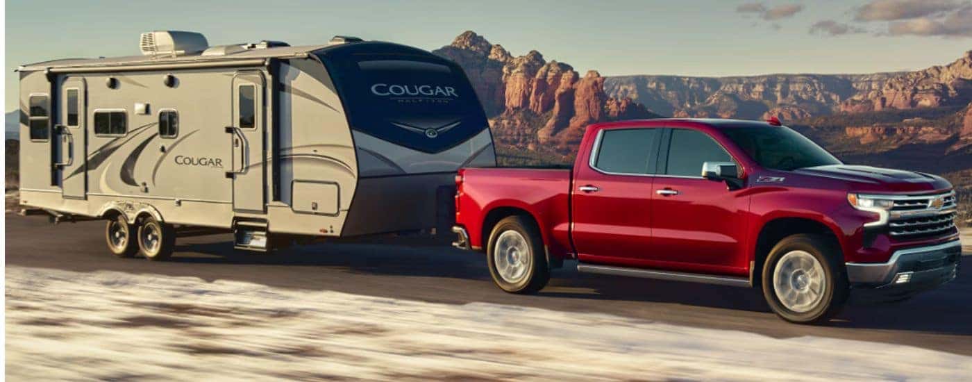 A red 2026 Chevy Silverado 1500 LTZ is towing a camper.