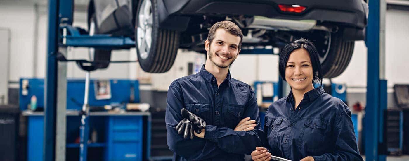 Two service technicians with a vehicle on a lift in the background.