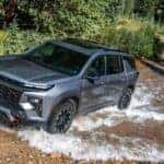 A gray 2026 Chevy Traverse Z71 driving through a dirt road puddle.