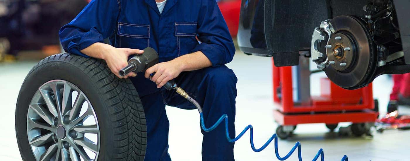 A mechanic kneeling near a tire in a garage.