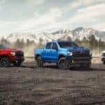 Three 2024 Chevy Silverado trucks - red, blue and white - parked in front of mountains.