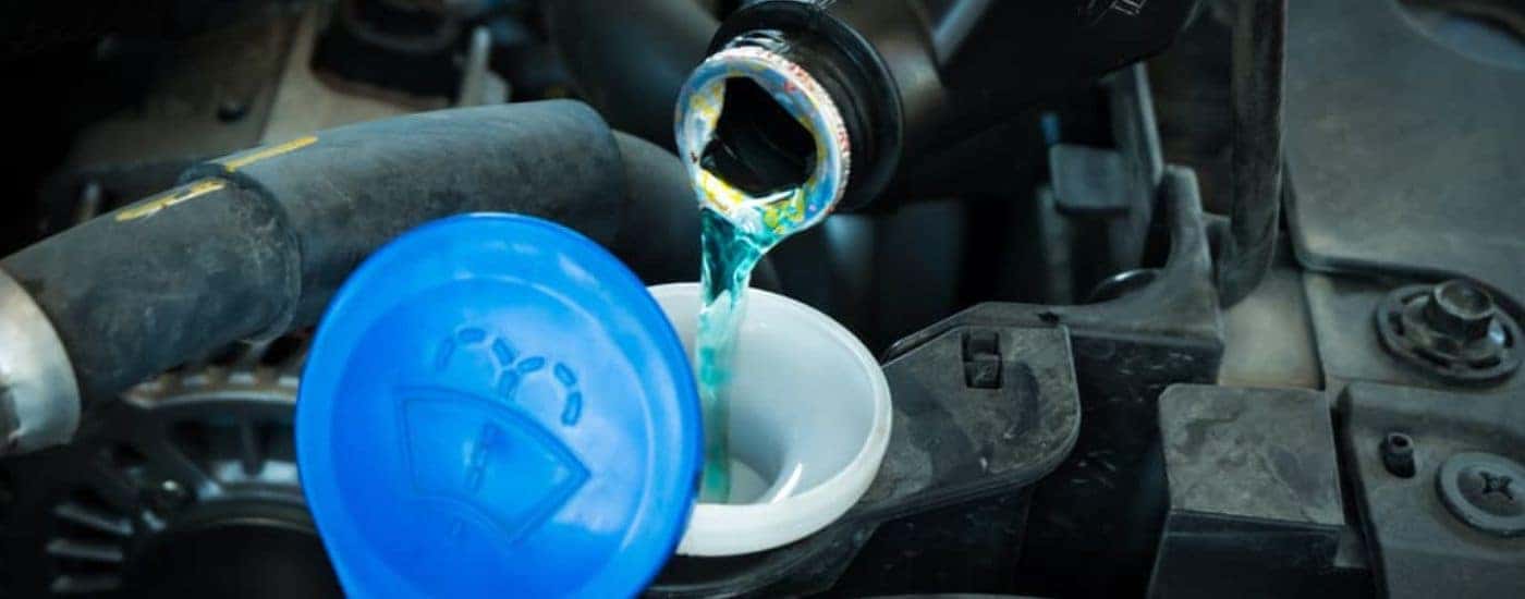 Windshield wiper fluid being poured into a vehicle.