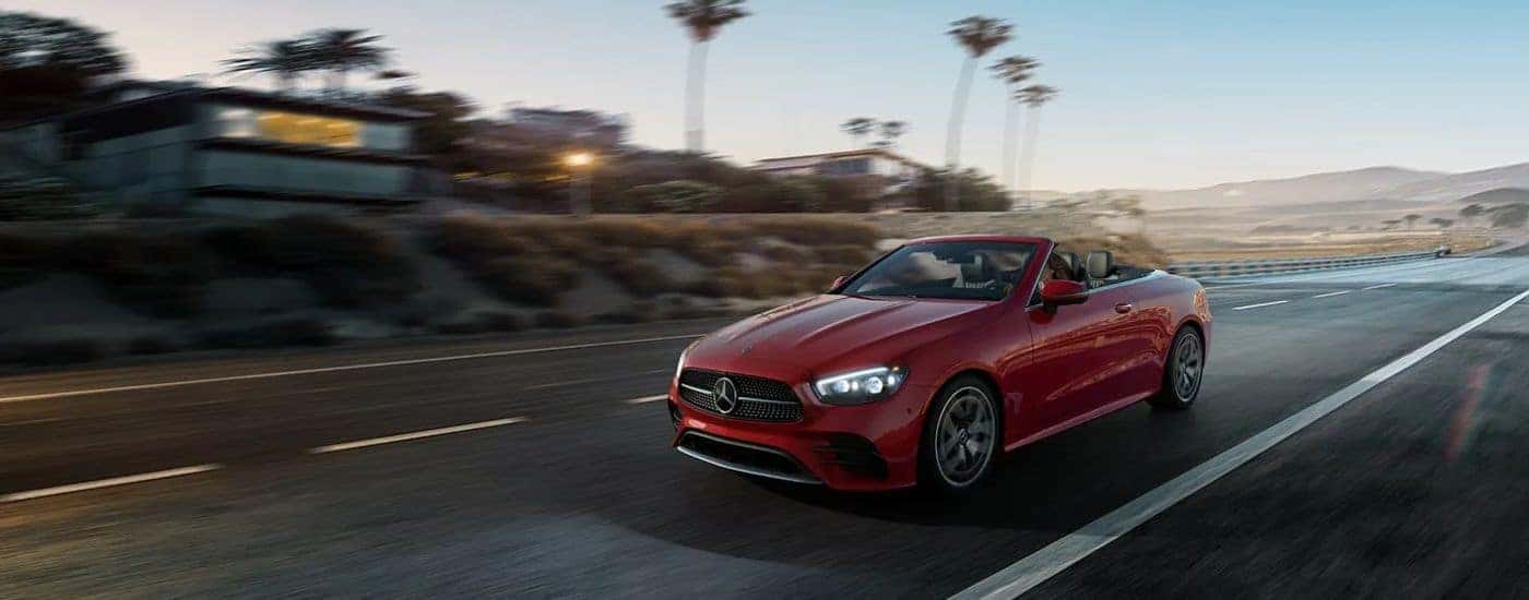 Red 2026 Mercedes-Benz E-Class Cabriolet driving down a street.