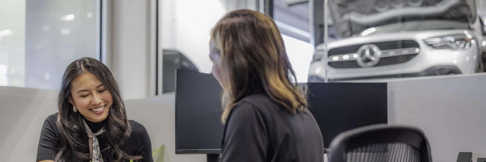 women smiling sitting down across from dealership employee
