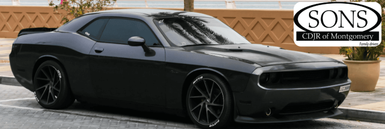 A photo of a black Dodge Challenger parked at a dealership portraying the diverse inventory of Dodge cars, trucks, and SUVs at SONS CDJR Fiat in Montgomery, AL.