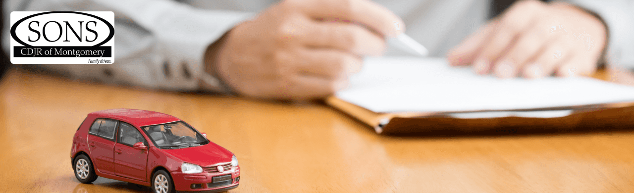 Person signing car trade-in paperwork with a toy car in the foreground
