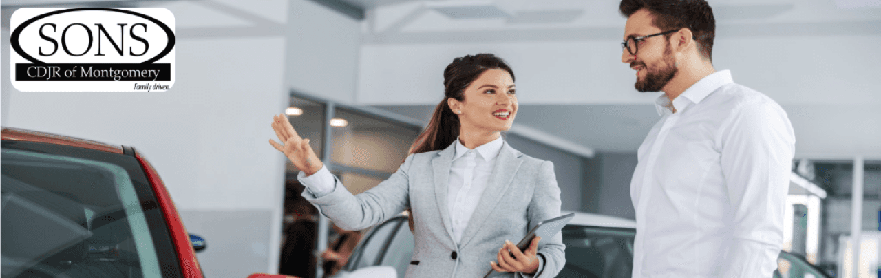 A bright, modern car dealership showroom with friendly salespeople and various new and used cars on display.