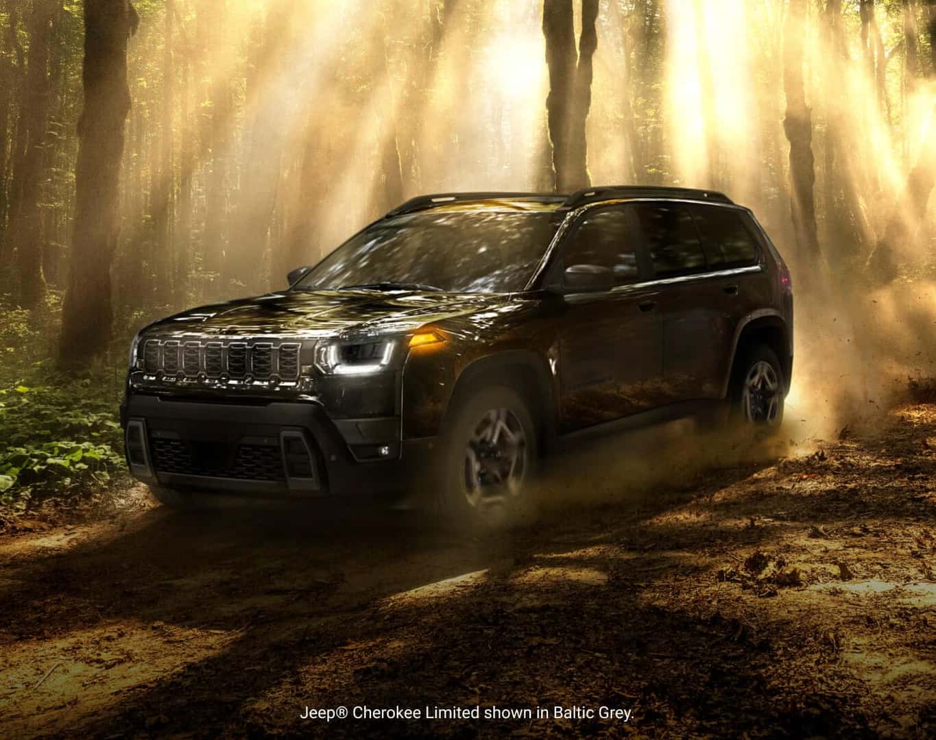 Front three-quarter motion view of a 2026 Jeep Cherokee Limited in Baltic Grey driving along a dusty forest trail.