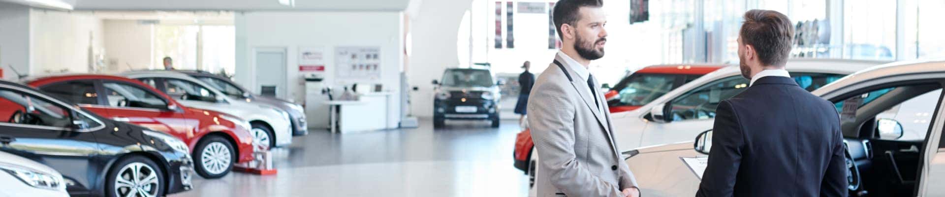Two sales representatives talking beside a vehicle inside a bright car dealership showroom.