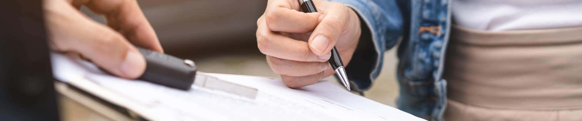 Customer signing paperwork on a clipboard while another person holds a car key fob.