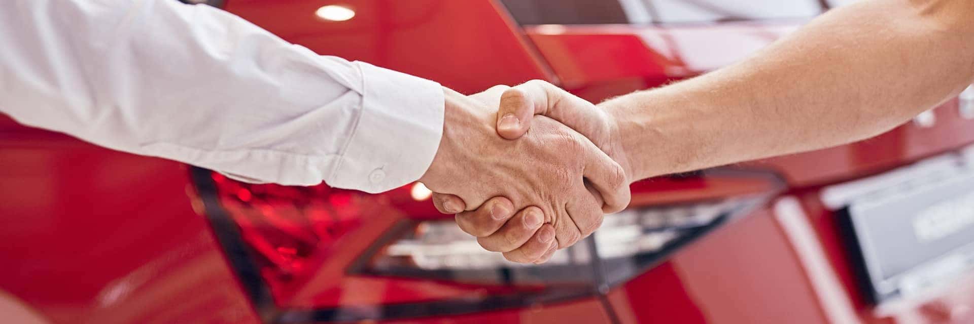 shaking hands in front of red vehicle