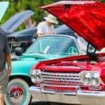 A man in black t-shirt standing beside a red car during a car show