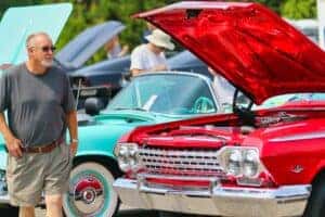 A man in black t-shirt standing beside a red car during a car show