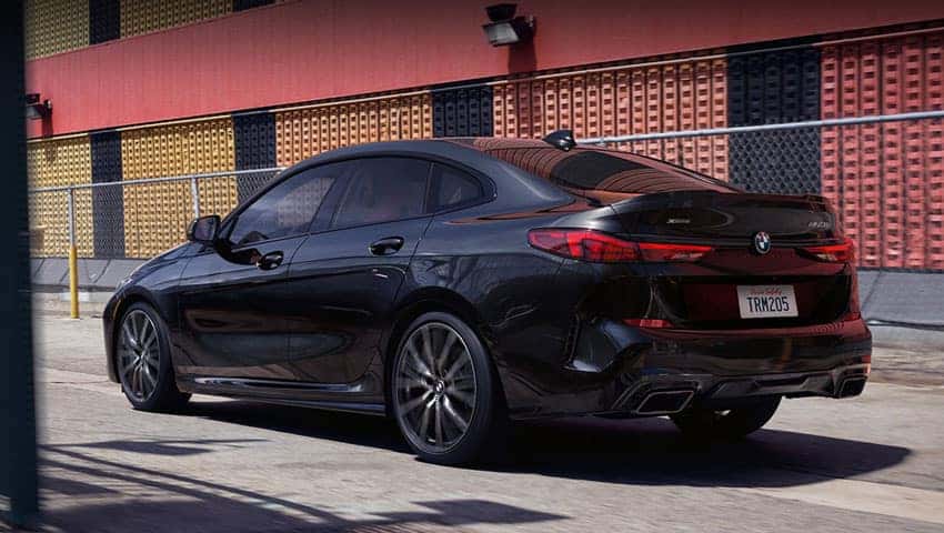 A black sapphire metallic BMW 2 Series Gran Coupe driving past a red and yellow building.