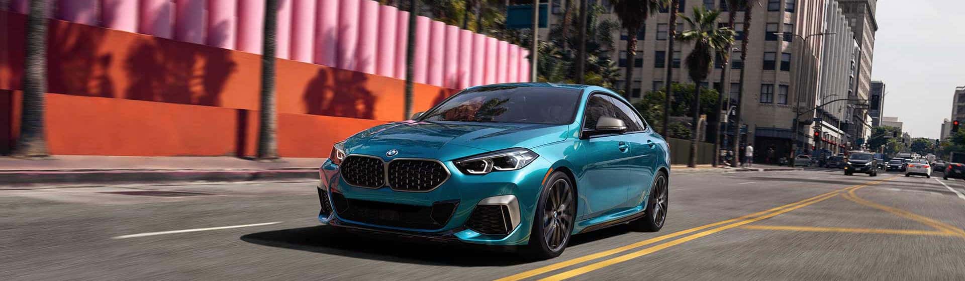 A blue metallic BMW 2 Series Gran Coupe driving down street during the day.