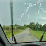 Flash of forked lightning in front of a car during a daytime thunderstorm