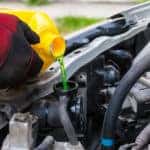 Gloved hand pouring coolant into a car