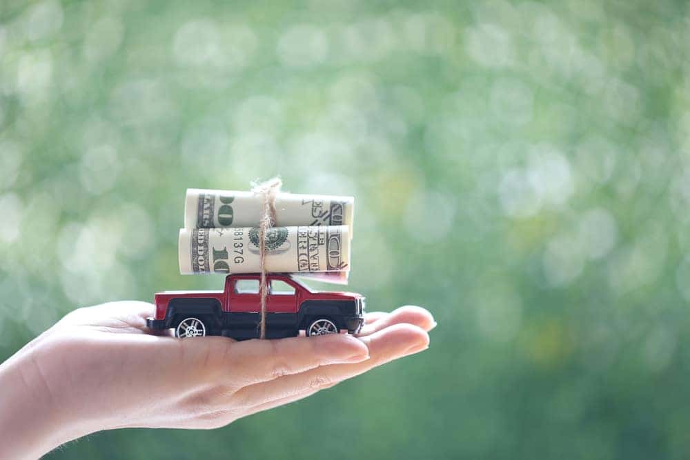 Hand holding a miniature truck with $100 bills rolled on top