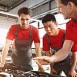 Three mechanics in red shirts fixing a car