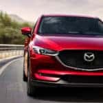 Red Mazda CX-5 cruising down tree-lined highway