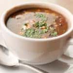 Cup of black bean and vegetable soup with a spoon on a saucer
