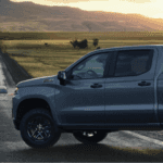 A gray Chevrolet truck against a field/farm at sunset.