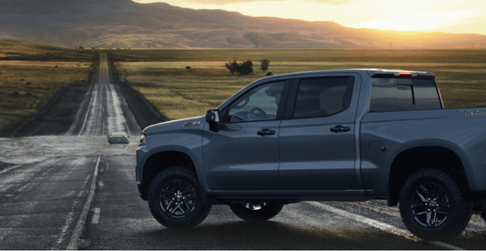A gray Chevrolet truck against a field/farm at sunset. 